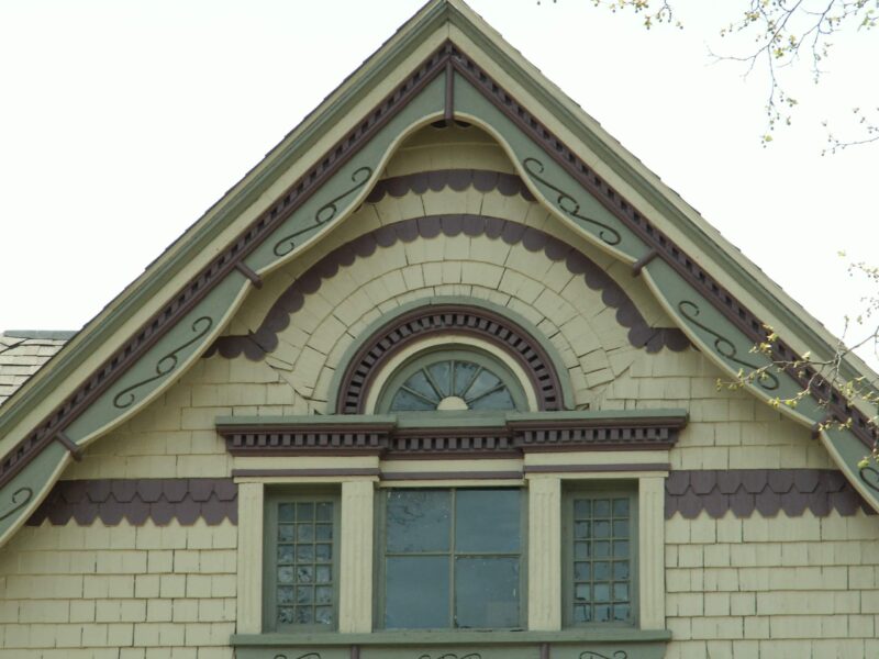 Victorian house exterior in Springfield, Ohio painted a variety of shades of green with maroon accent shingles and trim