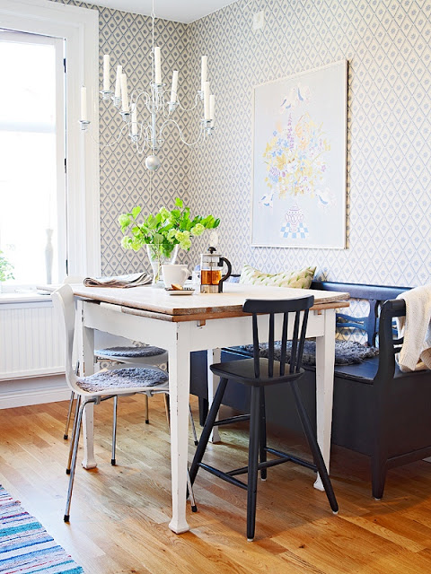 Kitchen in a small apartment with a chandelier, geometric wallpaper, blue bench, high table with mismatched chairs and a wood floor