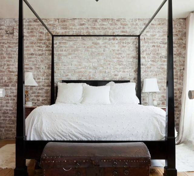 master bedroom with a dark wood canopy bed with a trunk at its foot with a brick wall providing the backdrop