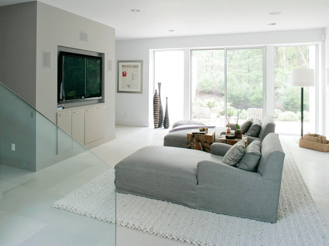 TV Room in the master suite in a modern farmhouse with a huge wall mounted tv, two long arm chairs, a white rug and a sliding door leading to a backyard