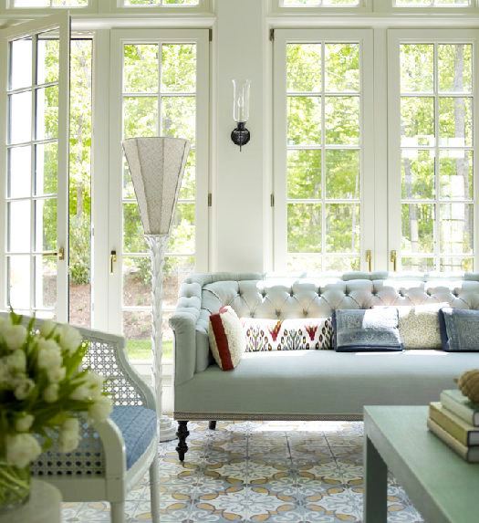 Living room with a tufted mint green sofa, Moroccan inspired patterned rug, a cane chair with a blue cushion, white french doors and a green coffee table in Katie Ridder's home