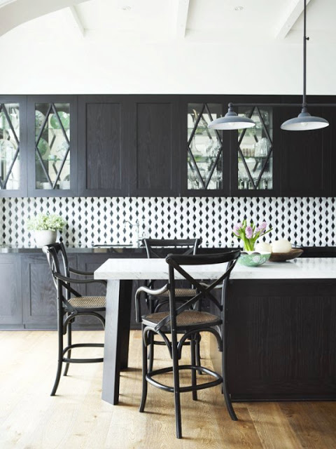 kitchen with dark wood cabinets, island with marble counter top, wood floors, pendant lights and a white black splash with black diamonds on it. 