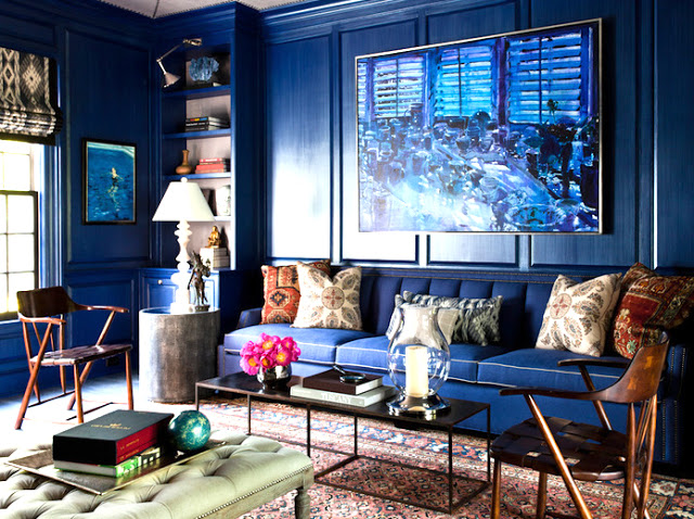 Library with blue walls with a large blue painting on the wall, a blue couch with patterned pillows and a Moroccan rug with blue accents