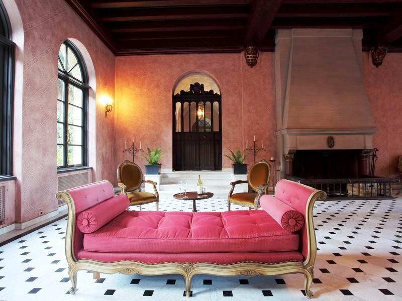 Alternative view of the music room in a Florentine style vila with a pink chaise lounge, two Louis XIV chairs, a large fireplace, pink walls and exposed beams