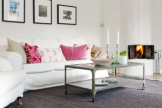 Living room in an apartment with a white sofa with pink accent pillows, a metal coffee table on wheels and a solid grey rug