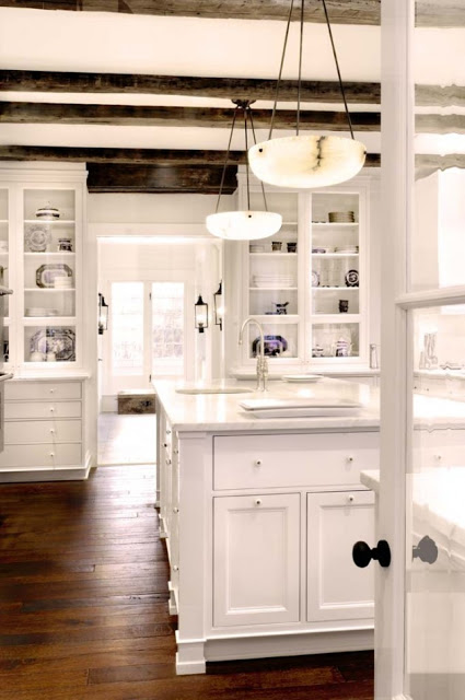 Kitchen with exposed beams, alabaster pendant lights hanging above the kitchen island, white cabinets and a wood floor