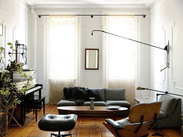 living room with white walls etched rectangle wall modling, wood floors, a piano, gray sofas and a black leather ottoman chair