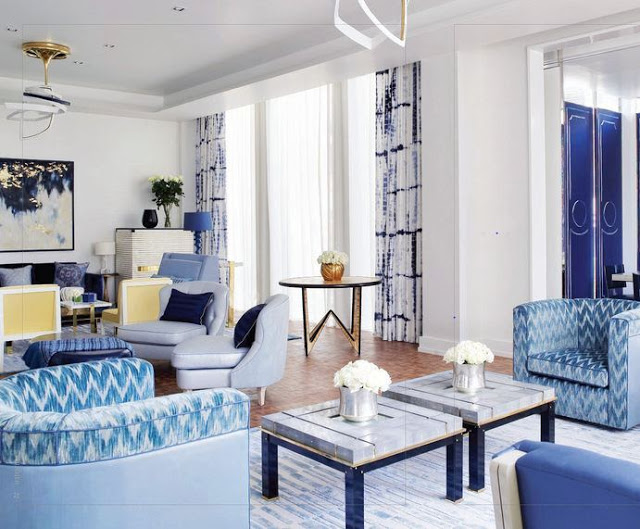 living room in bangkok with blue and white chevron printed armchairs, lacquer doors, a wood floor, floor length blue and white tie dye curtains and marble coffee table