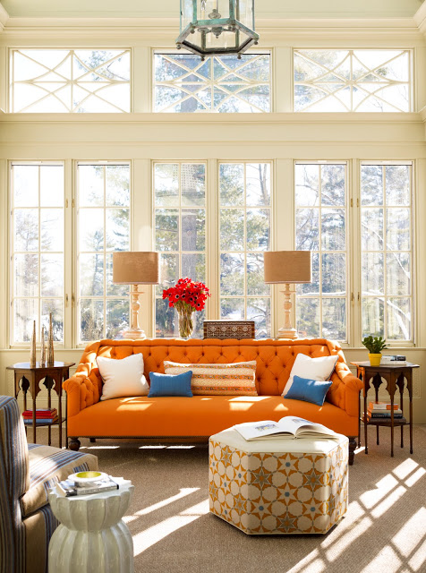 Living room with an orange sofa, tall windows, a hexagon ottoman, a striped armchair and Moroccan style side tables