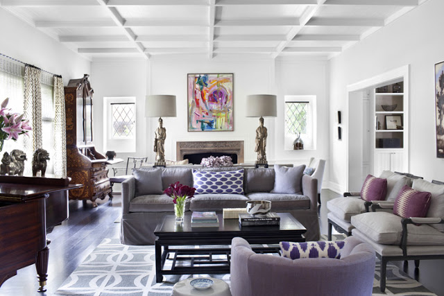 Living room in Tudor style home with gray sofas with purple accent pillows, statuette lamps and a piano