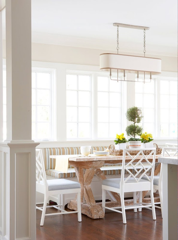 Breakfast nook with banquette seating, a chandelier, a reclaimed wood table surrounded by white chairs, and casement windows