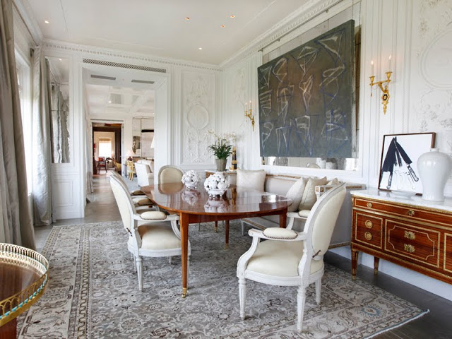 Dining room with large area rug, wood table, white louis xiv chairs, white molded walls and modern art