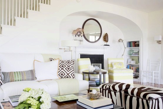 beach cottage with chic zebra ottoman, white sofa, upholstered striped chairs, fireplace with a round mirror on the mantel, and a tortoise shell