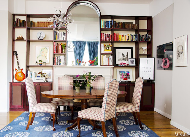 Dining room with Madeline Weinrib rug, a large oval table, plaid upholstered chairs, a pass through window to the kitchen with wooden bookcases holding books, art and other small items