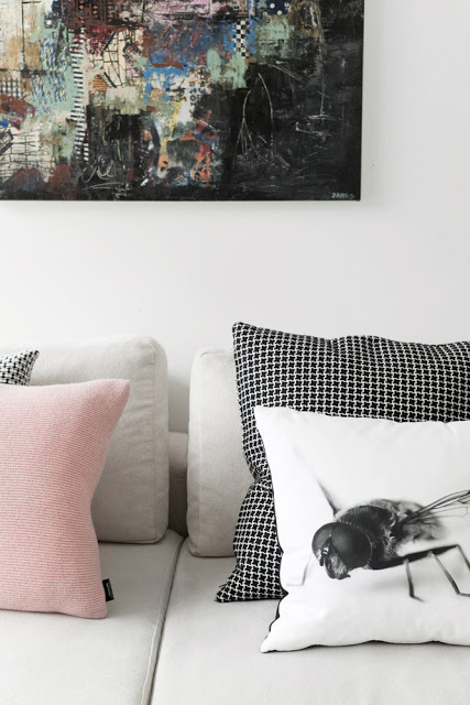 close up of a living room by bo bedre with a light gray sofa with black and white check pillows, a pink pillow and a white pillow with a large fly printed on it