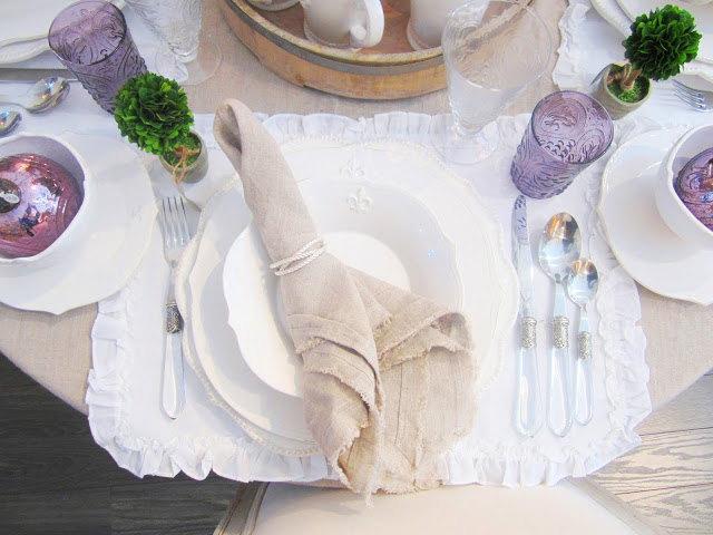 Close up of place setting with lavender glass, linen napkin, white placemats and silverware