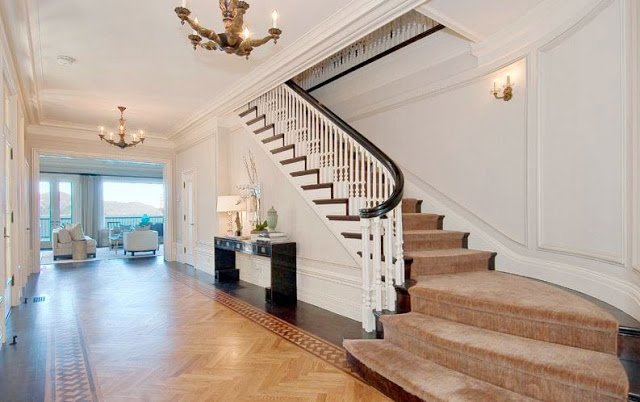 foyer with a herringbone inlay and a view into the living room and ocean. A grand staircase with carpeting and two chandeliers