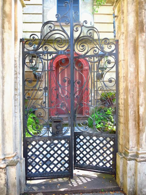 Scrolling wrought iron gate and an arched red door with checkered marble path in Charleston, South Carolina