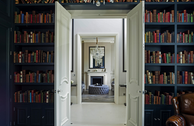 Blue library in a suburban London home with built in bookshelves and leather club chairs