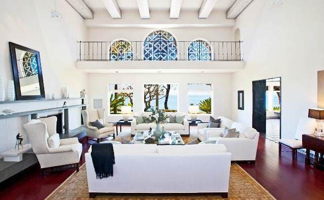 living room with hard wood floor, white dueling sofas and armchairs, a large area rug, a fireplace and a large mirror on the mantel with a view of the second level and the ocean