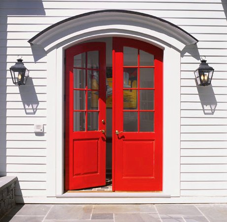 Exterior of a white house with curved, bright red door, two lantern lights on each side of the door and a stone tile walkway