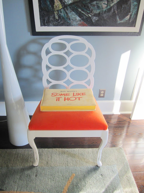 Glossy white Elkins chair with bright orange upholstered seat with a copy of "Some Like It Hot"