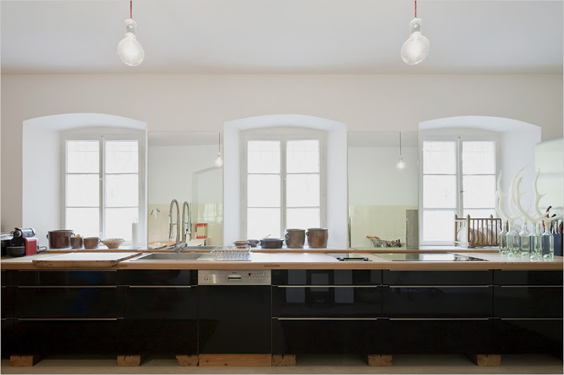 Kitchen in the Hammerhaus castle with glossy black cabinets with long drawer pulls, a wood countertop and two pendant lights
