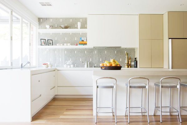 kitchen with two toned cabinets, white island, silver stools with low backs, wood floors and a black and white backsplash