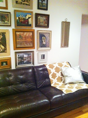 COCOCOZY Gate throw in tan on a dark brown leather sofa in front of a wall full of framed pieces of art in a readers home