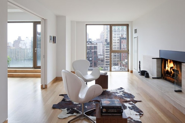 fireplace room in a New York City apartment with light wood floors, a cow skin rug, two white chairs and a great view of the city