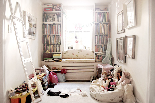 Window seat in a girl's playroom with stuffed animals, a bean bag chair, and two built in book cases stuffed with books
