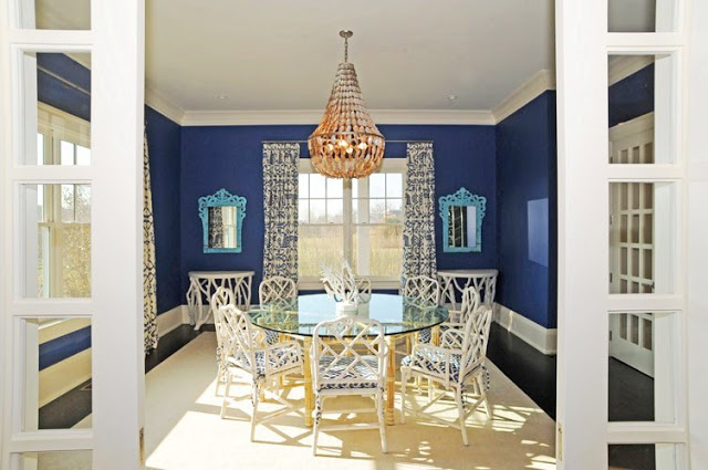 dining room with blue walls with white trim, a chandelier, french doors with blue and white curtains, dark wood floor, a round table with a glass top and white wood chairs with blue and white cushions