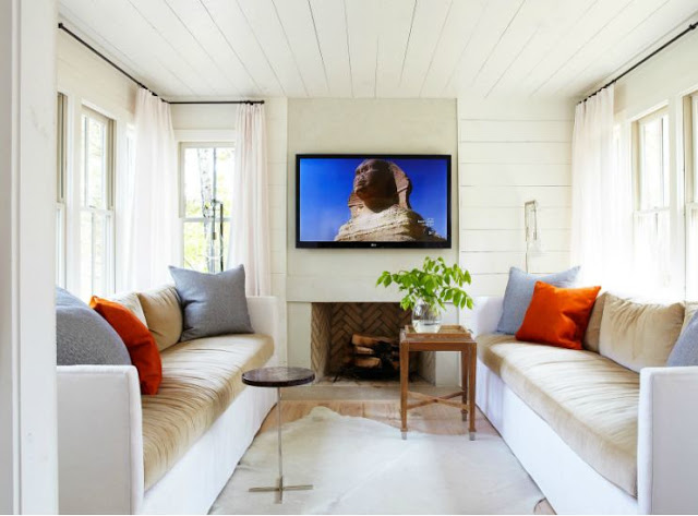 television tv room with dueling two toned sofas, white wood slat ceiling, fireplace, animal skin rug with a wood side table 