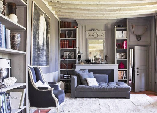 Grey French living room with exposed beam ceiling, wood floor, large grey area rug, built in bookshelves, Louis XVI armchair and a chaise lounge sofa