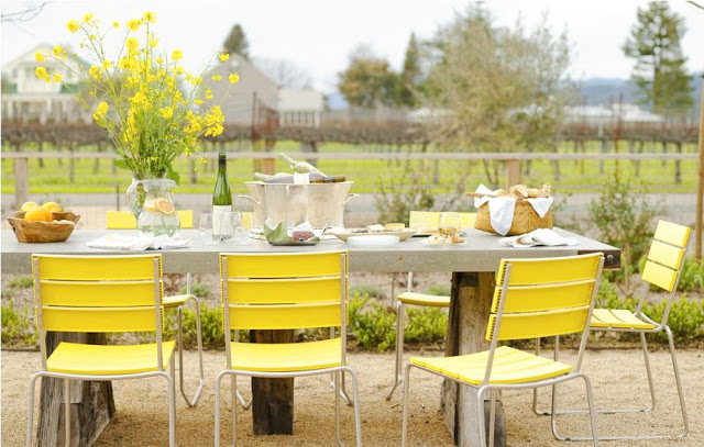 Lemon yellow outdoor chairs surrounding a metal picnic table set for lunch al fresco on the edge of a vineyard