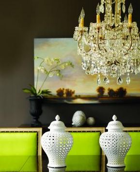 Dark dining room with dark brown walls, a large landscape painting, a crystal chandelier, bright apple green upholstered chairs, and two white lattice pots on a dark table