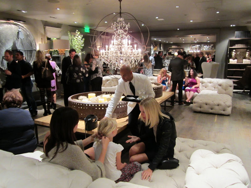 People mingling at the new Restoration hardware on white fully tufted sofas and sectionals