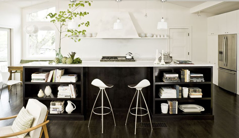 Sleek kitchen with dark wood floor, white counter tops, a dark wood island has open shelves holding books and other small objects, two white pendant lights and floating shelves on the back wall on both side of the hood