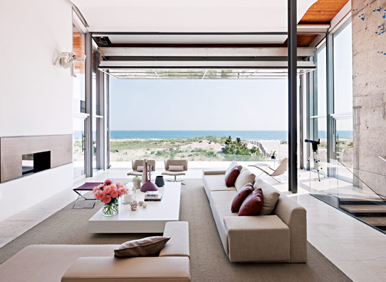 ultra modern living room with retractable wall, fireplace, long sofa and armchair with a view of the ocean