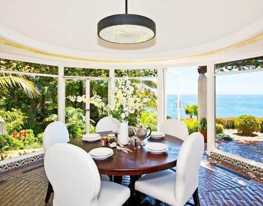 breakfast nook with tile floor, round wood table surrounded by white upholstered chairs and glass walls showing off the beautiful ocean and garden views