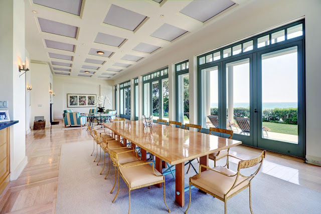 dining room with high coffered ceiling with a long wooden table surrounded by yellow chairs with glass doors and windows with an ocean view