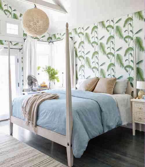 Beachy bedroom with a white four poster bed and floor to ceiling palm inspired wallpaper 