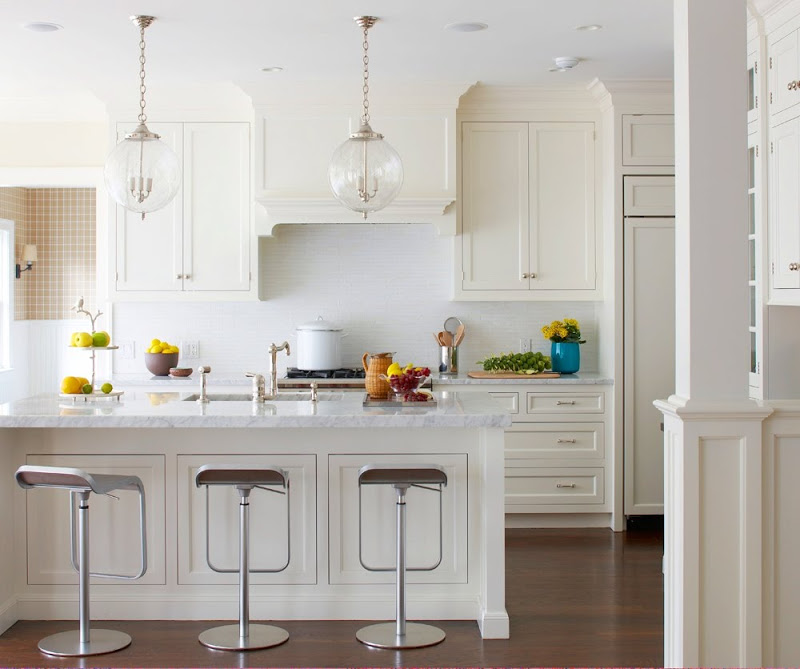 White kitchen with two pendant lights, silver bar stools and a hard wood floor