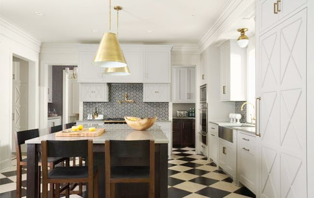 Kitchen with pinwheel tile backsplash, white cabinets and drawers, black and white checkered floor, brass pendant lights over and island surrounded by wood bar stools with leather cushions