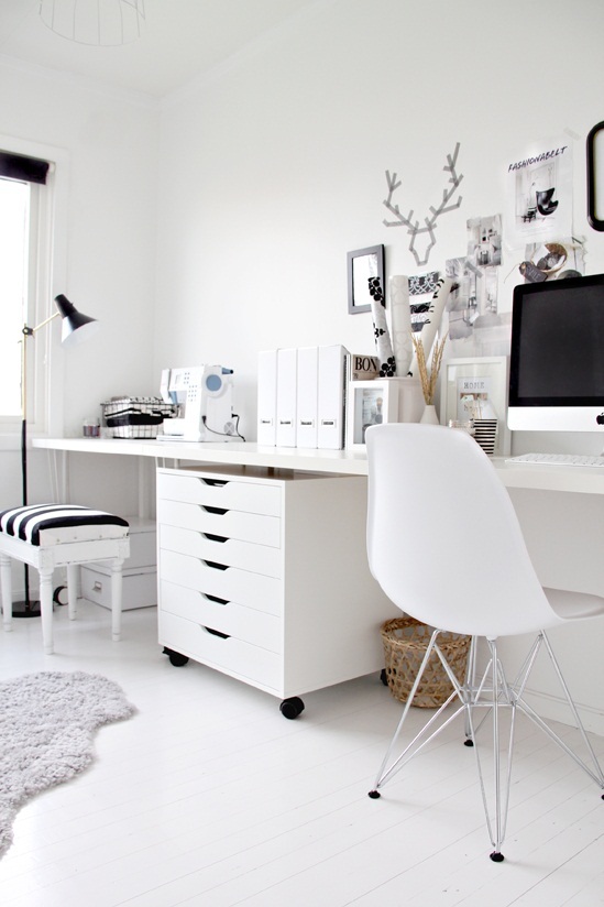 white home office with eames chair, white desk, white rolling chest of drawers with black accents in the form of pictures frames and a striped stool