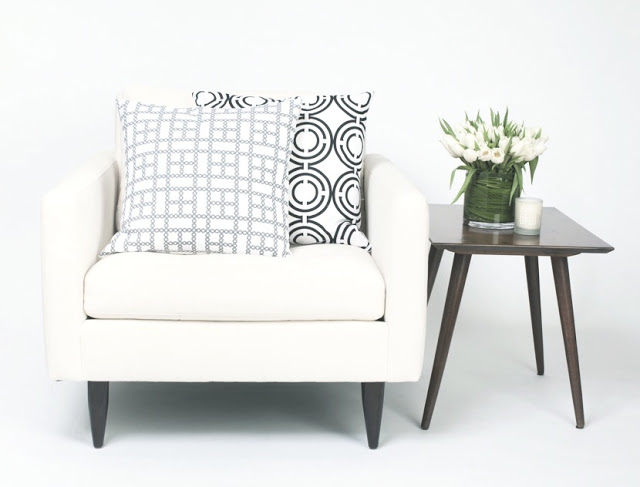 COCOCOZY Light pillows on a white chair with a wood accent table holding white tulips and a candle