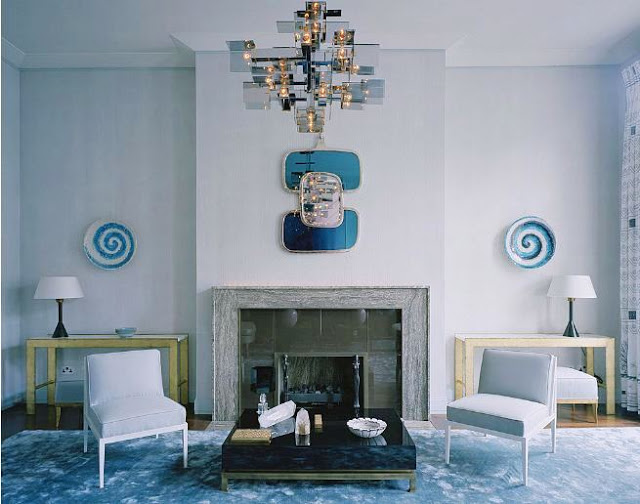 Alternative view of the living room with a fireplace, grey walls, a small mirror, two lavender chairs, a low coffee table and decorative plates as wall decor