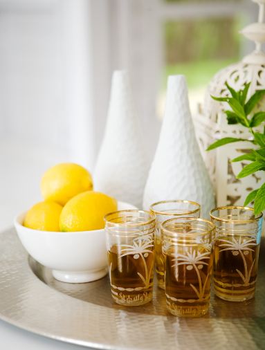 Close up of a silver tray holding 4 gold tea glasses full of tea, a white bowl of lemons and two white vases