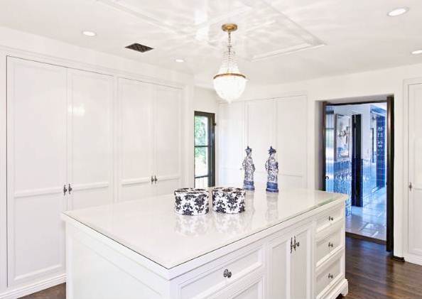 dressing room with crystal pendant light, white cabinets and a white island with two small statues and decorative boxes
