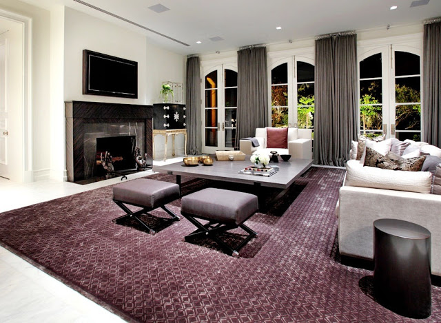 Den in a mansion on Harbor Island, in Newport Beach with french doors, gray floor length curtains, a large purple rug, gray coffee table, gray sofa and a large marble fireplace